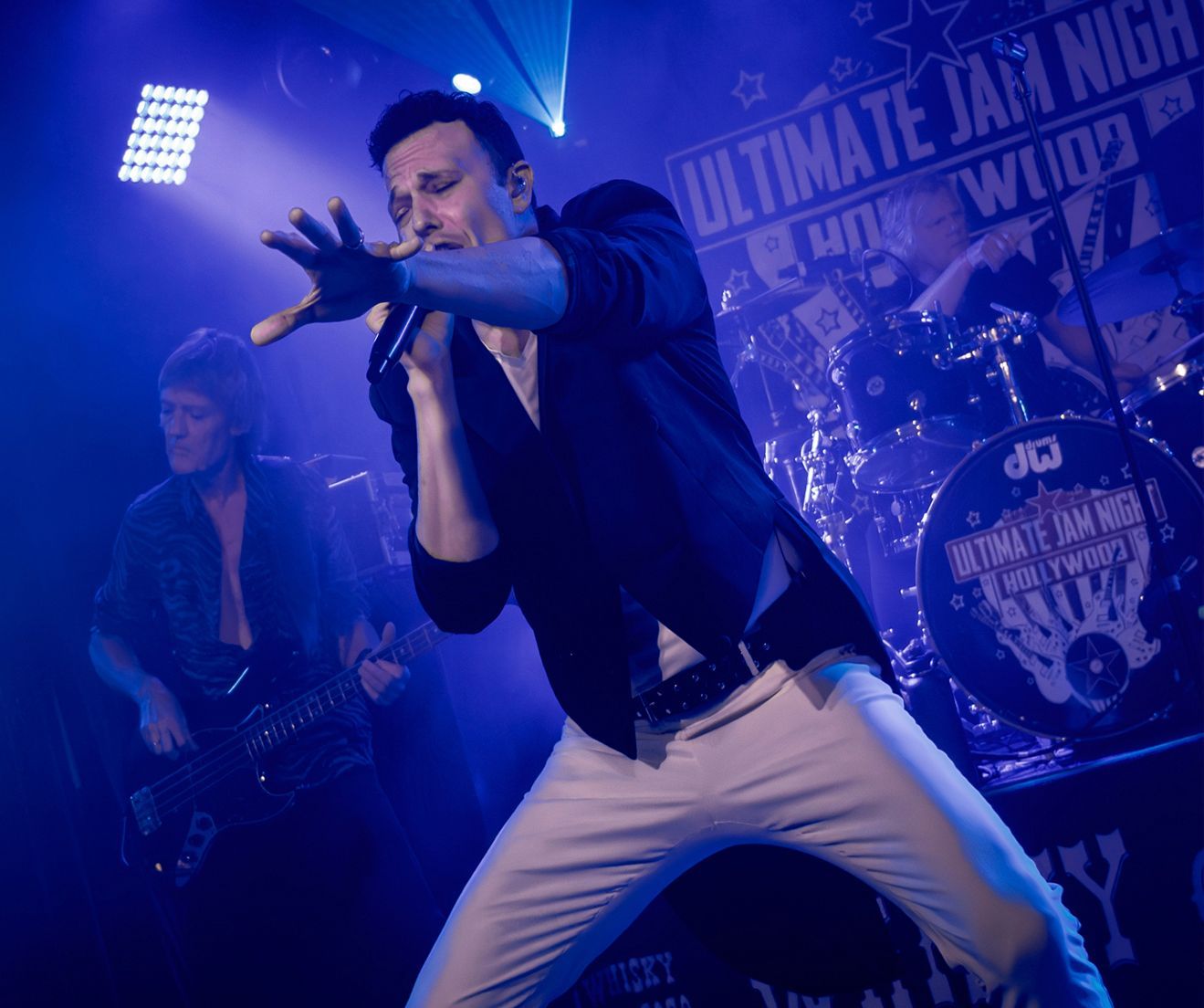 A man singing into a microphone in front of a sign that says ultimate jam night