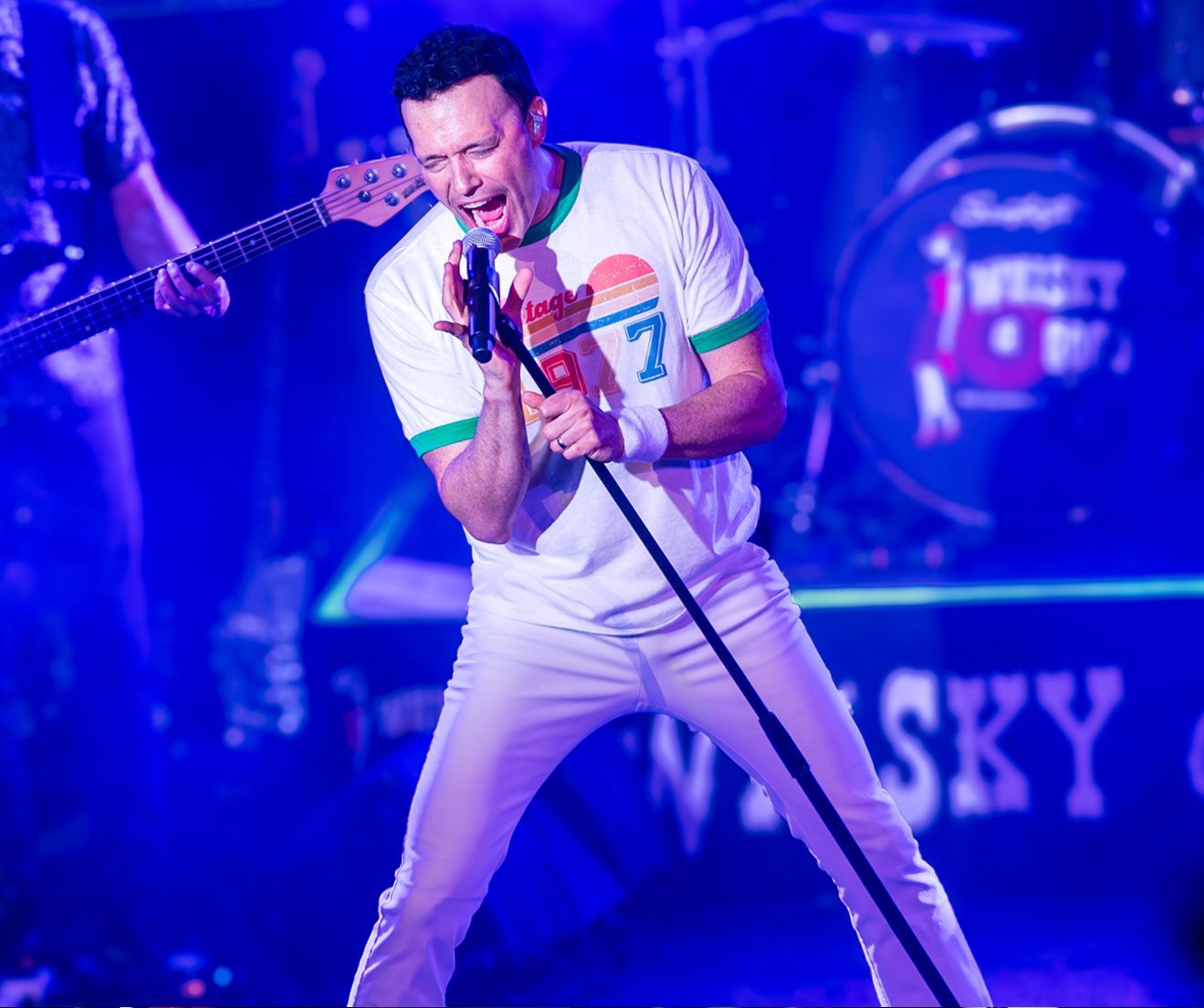 A man is singing into a microphone while playing a guitar on stage.