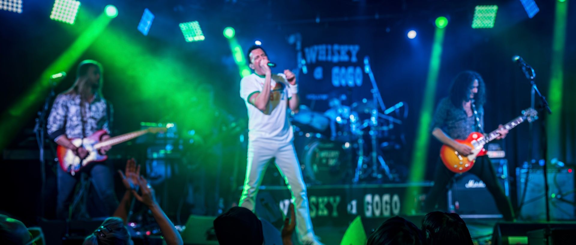 A man is singing into a microphone on a stage while two men play guitars.