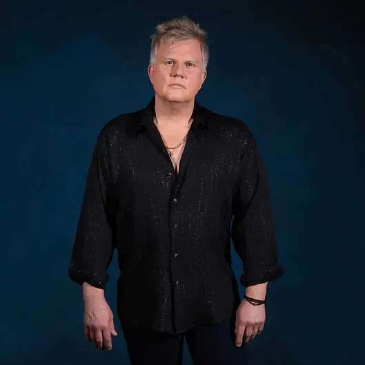glenn jost in a black shirt is standing in front of a blue background.
