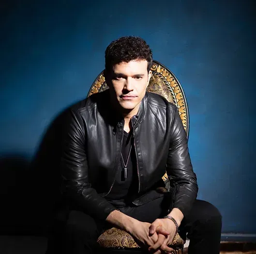 paulie z in a black leather jacket is sitting in a chair.