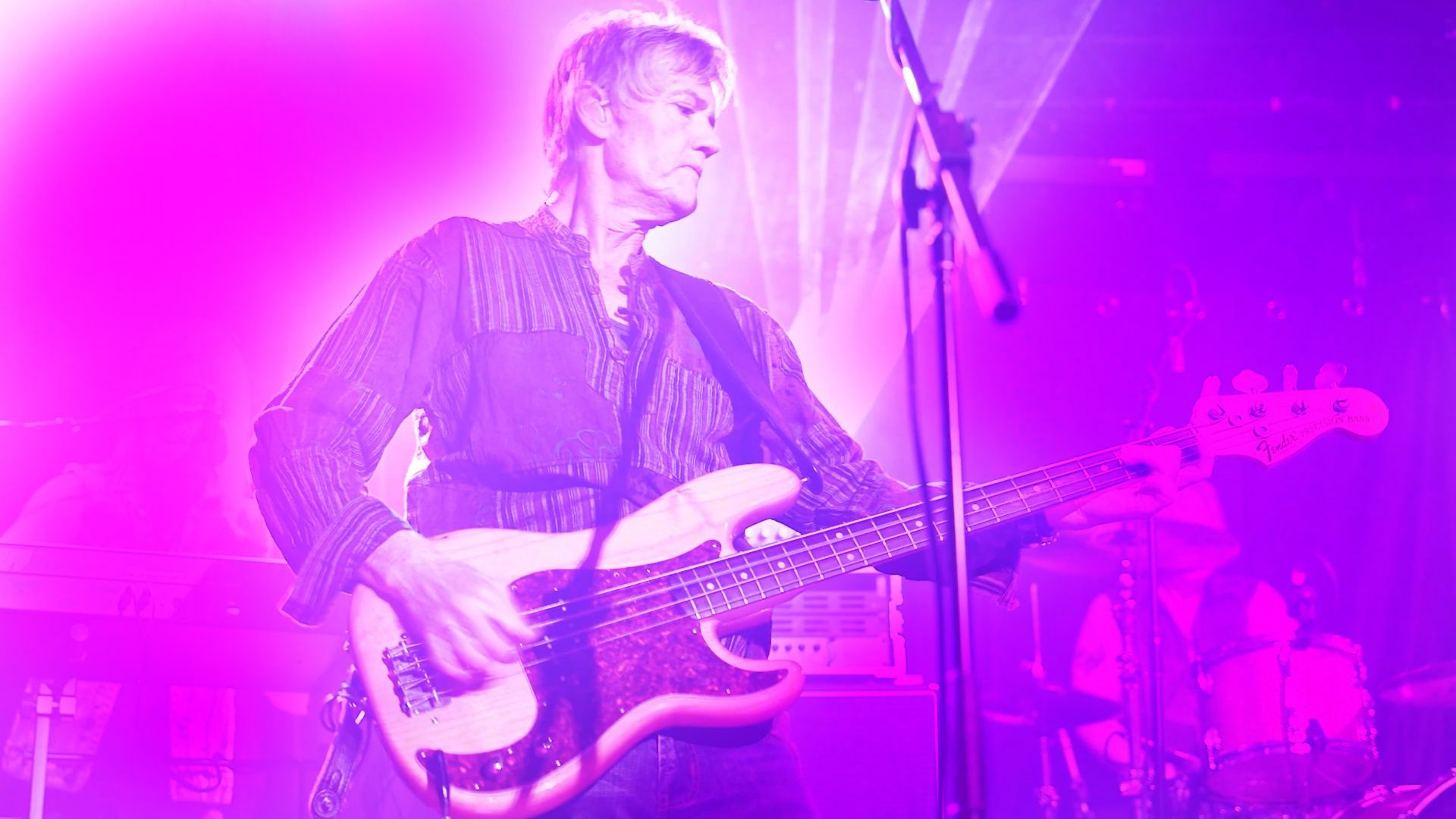 A man is playing a guitar on a stage in front of a microphone.