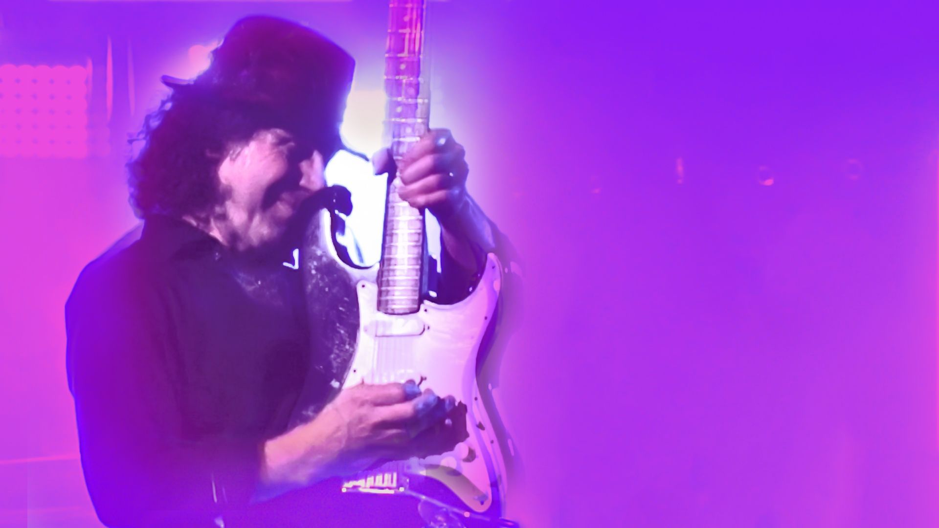 A man in a top hat is playing a guitar on a stage.