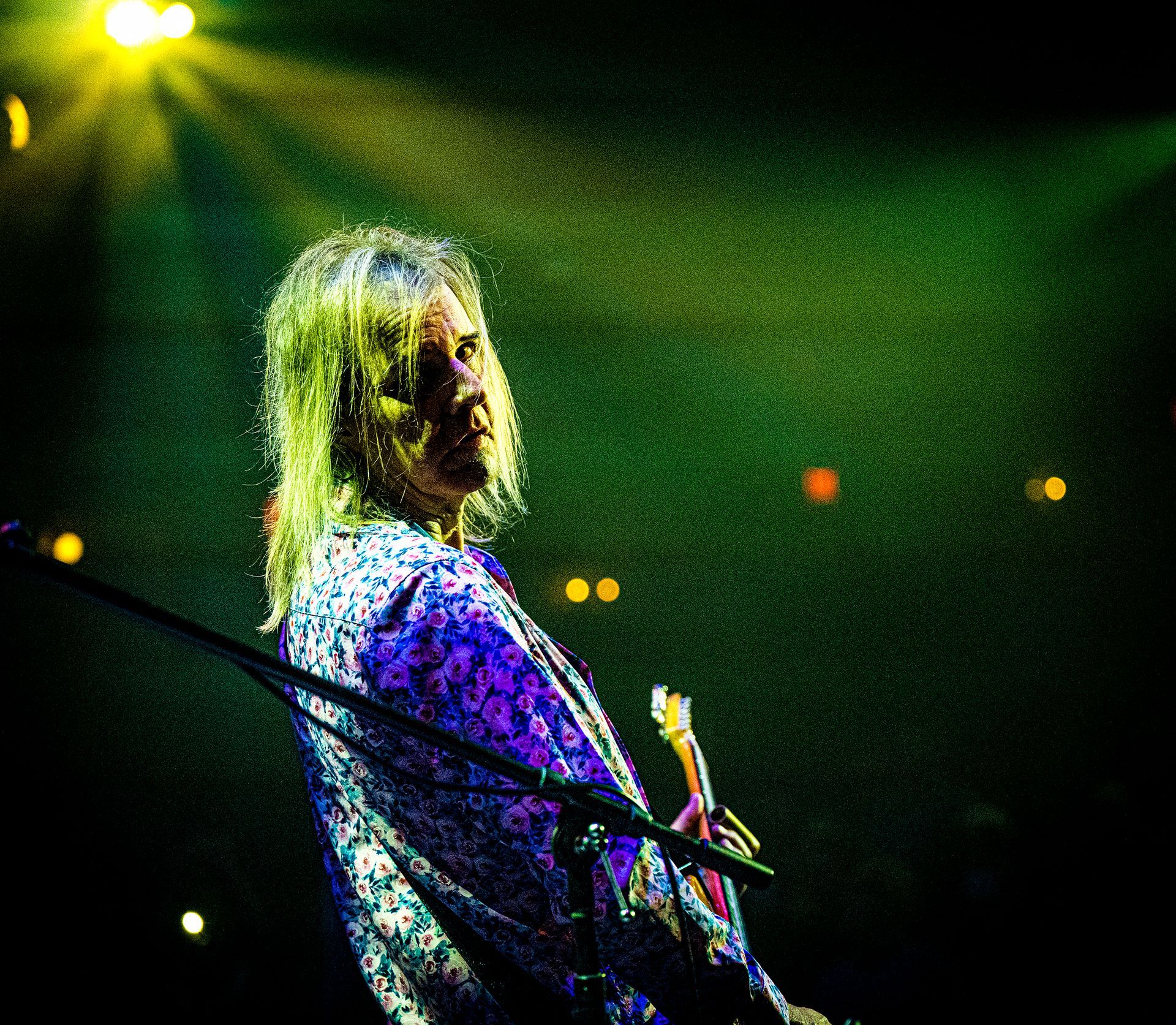 A man in a purple shirt is playing a guitar on stage
