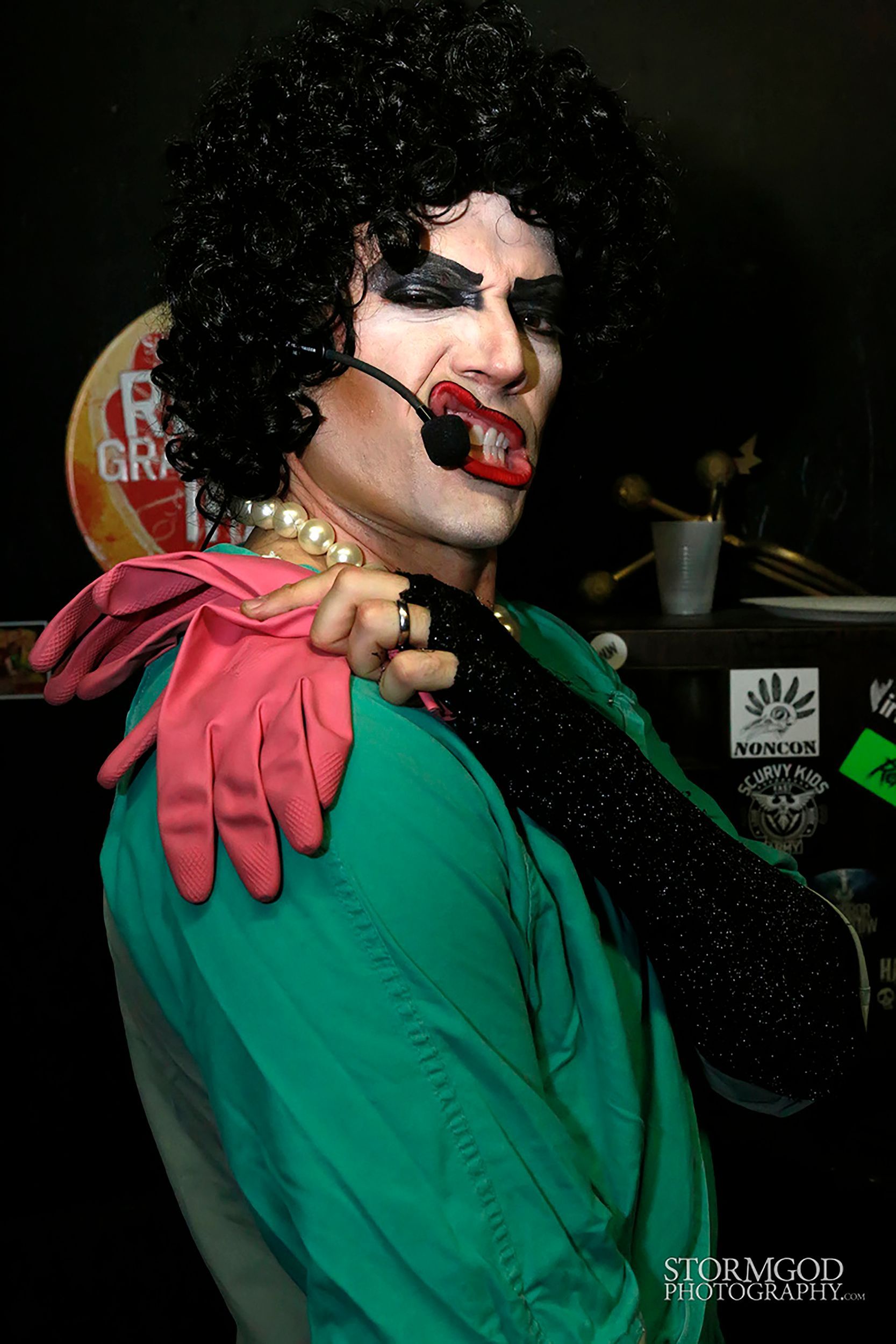 A man in a drag queen costume is holding a pink glove over his shoulder