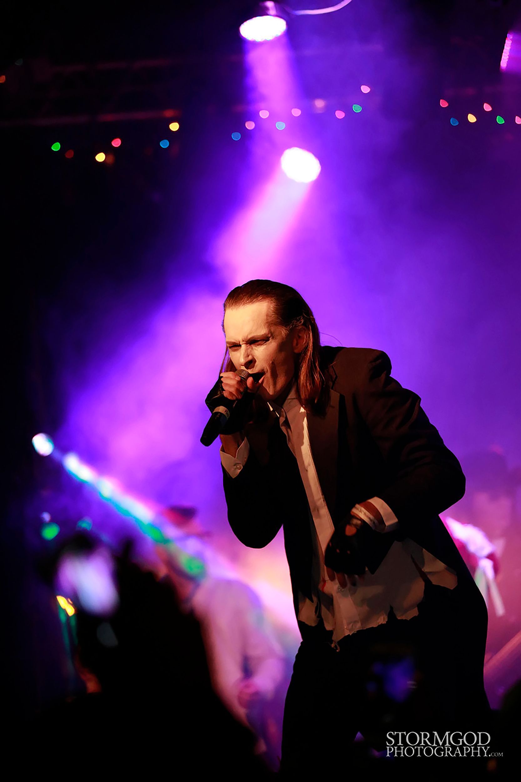 A man singing into a microphone with purple lights behind him
