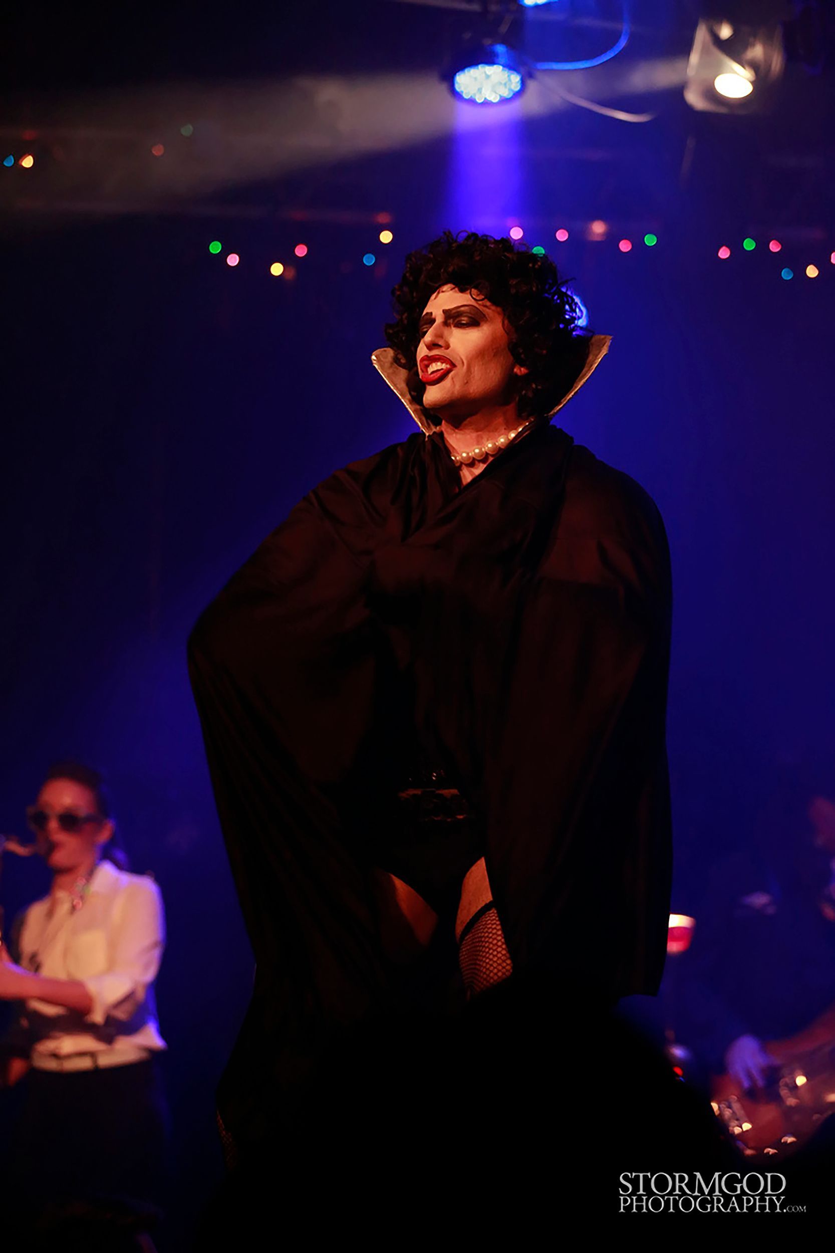 A man in a black cape is standing on a stage