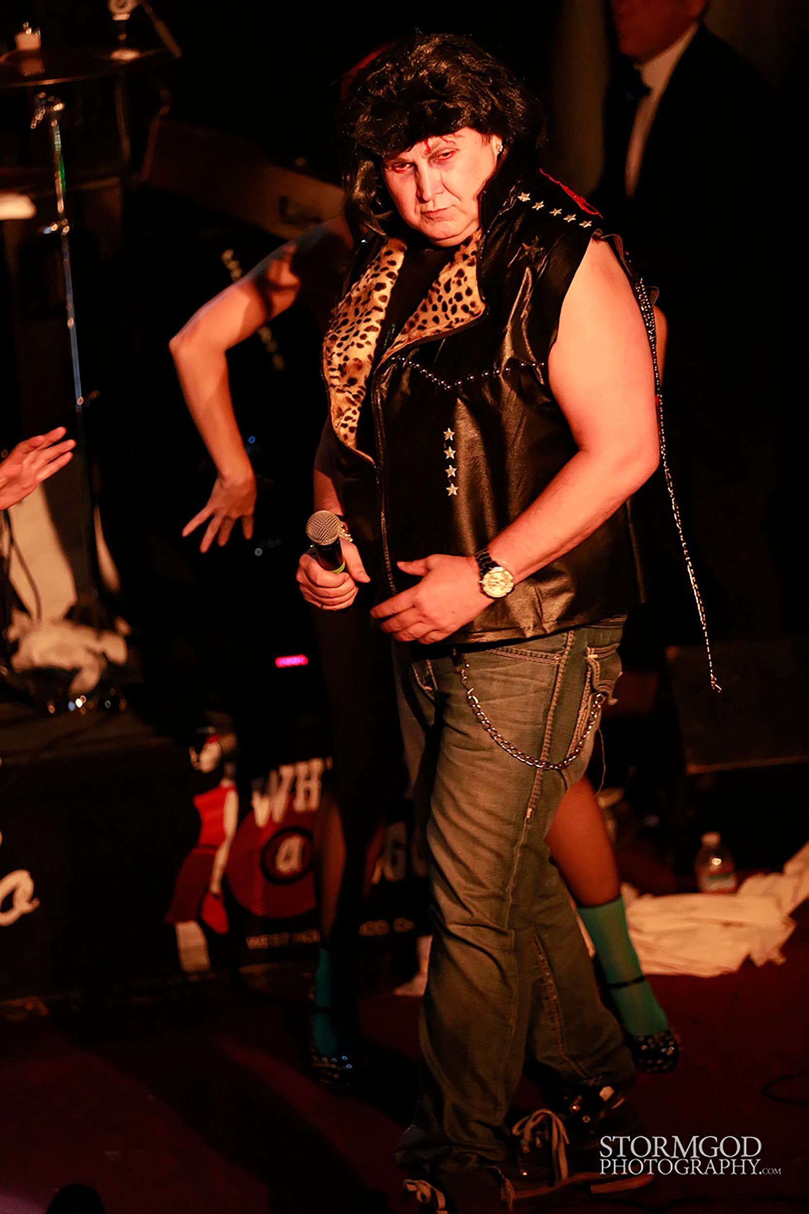 A man in a leopard print vest is holding a microphone