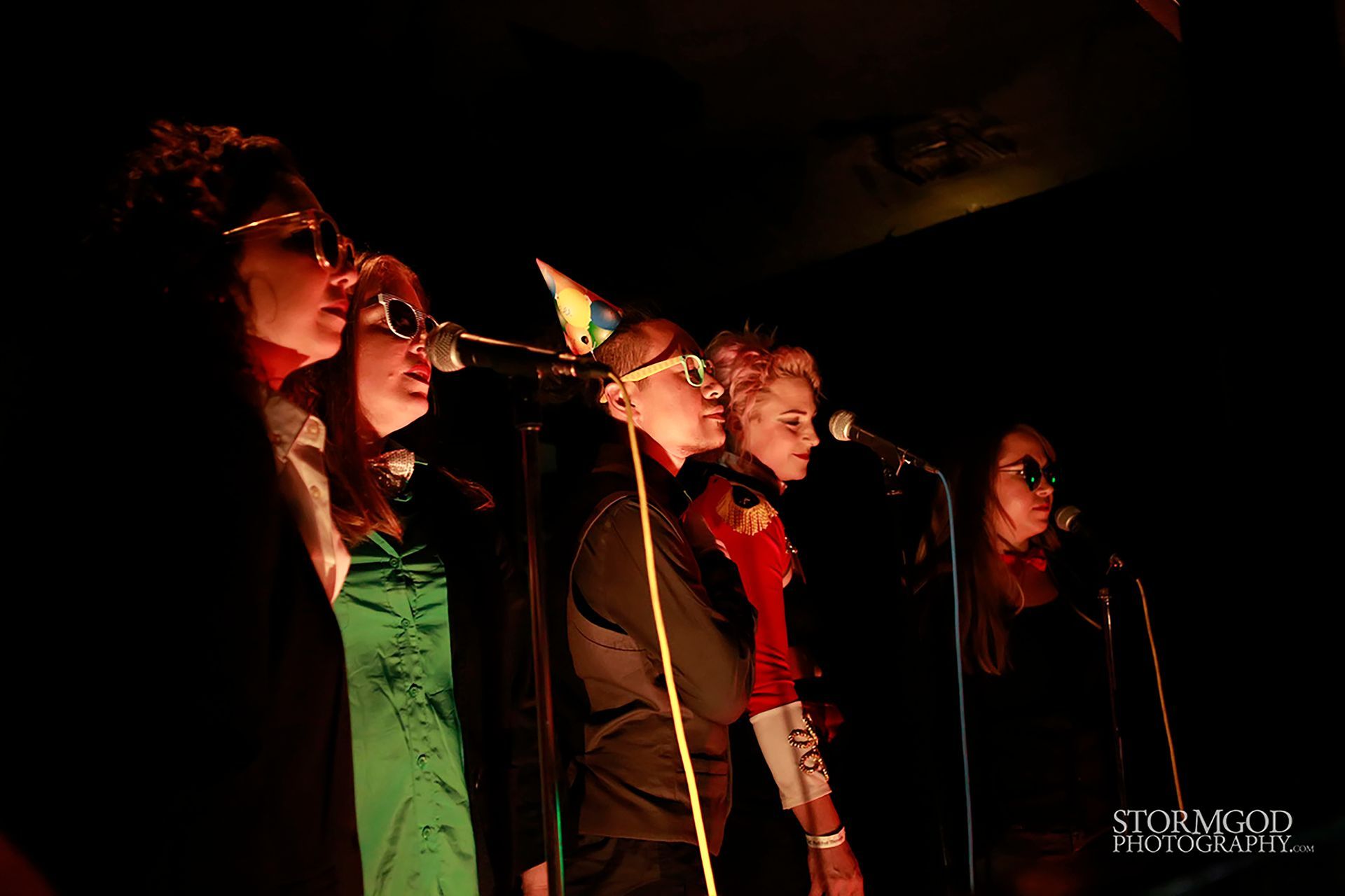 A group of people singing into microphones in a dark room.