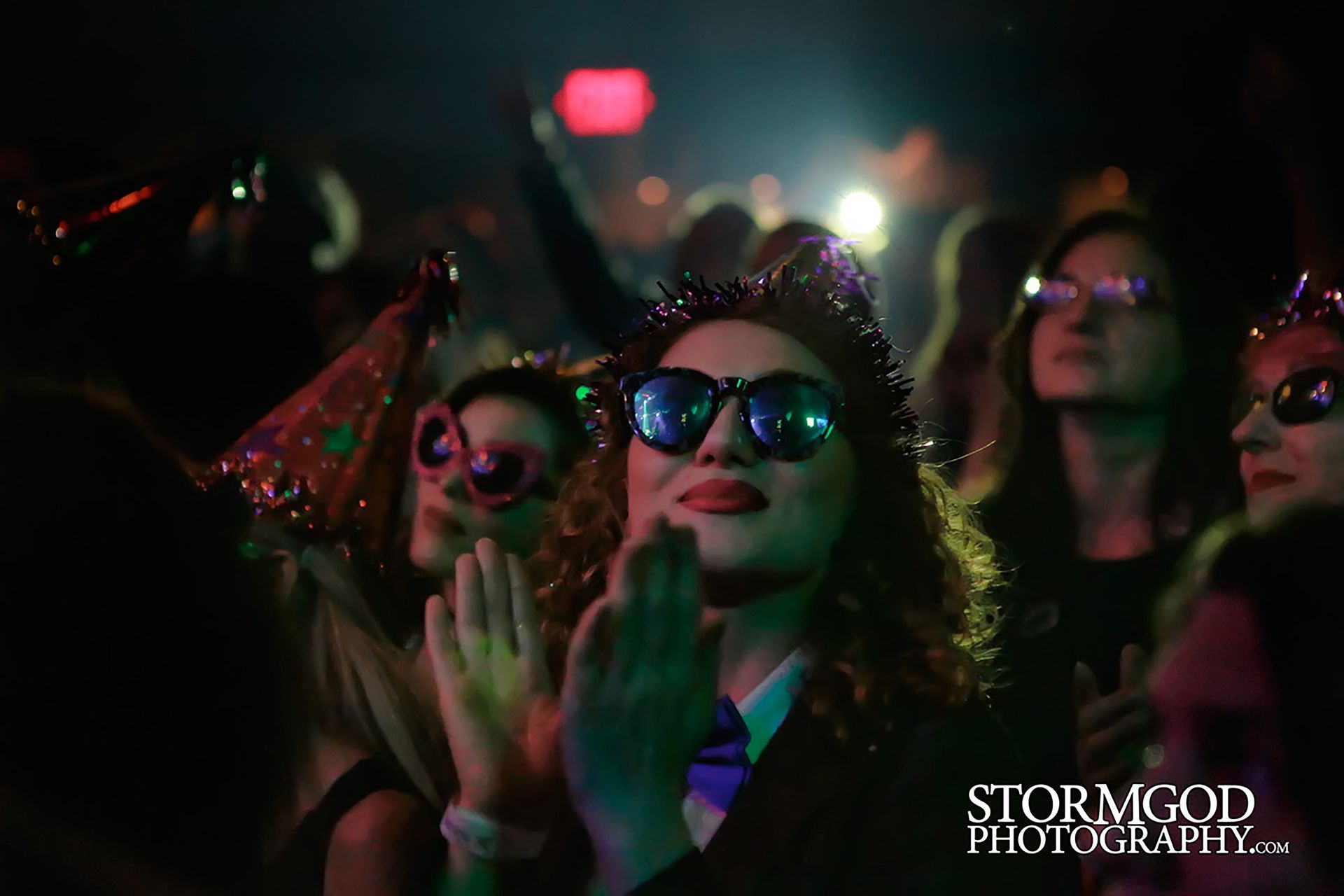 A group of people wearing sunglasses and party hats are standing in a dark room.