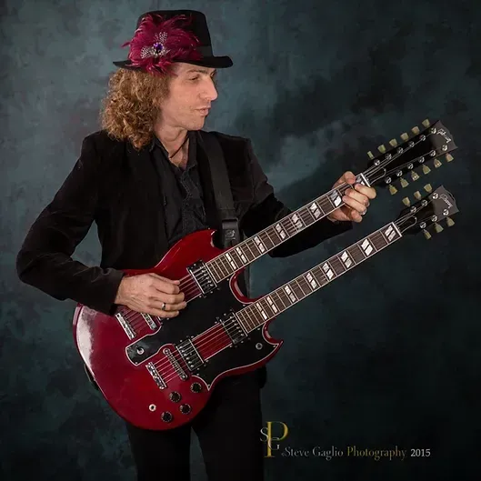 steve zukowsky in a hat is playing a double neck guitar