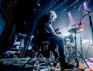 Drummer playing on stage, illuminated by stage lights.