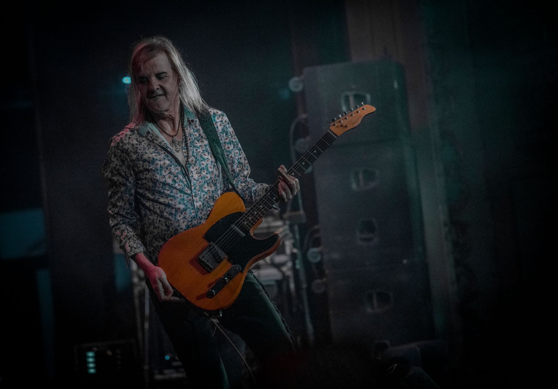 A man is playing a guitar on stage in a dark room.