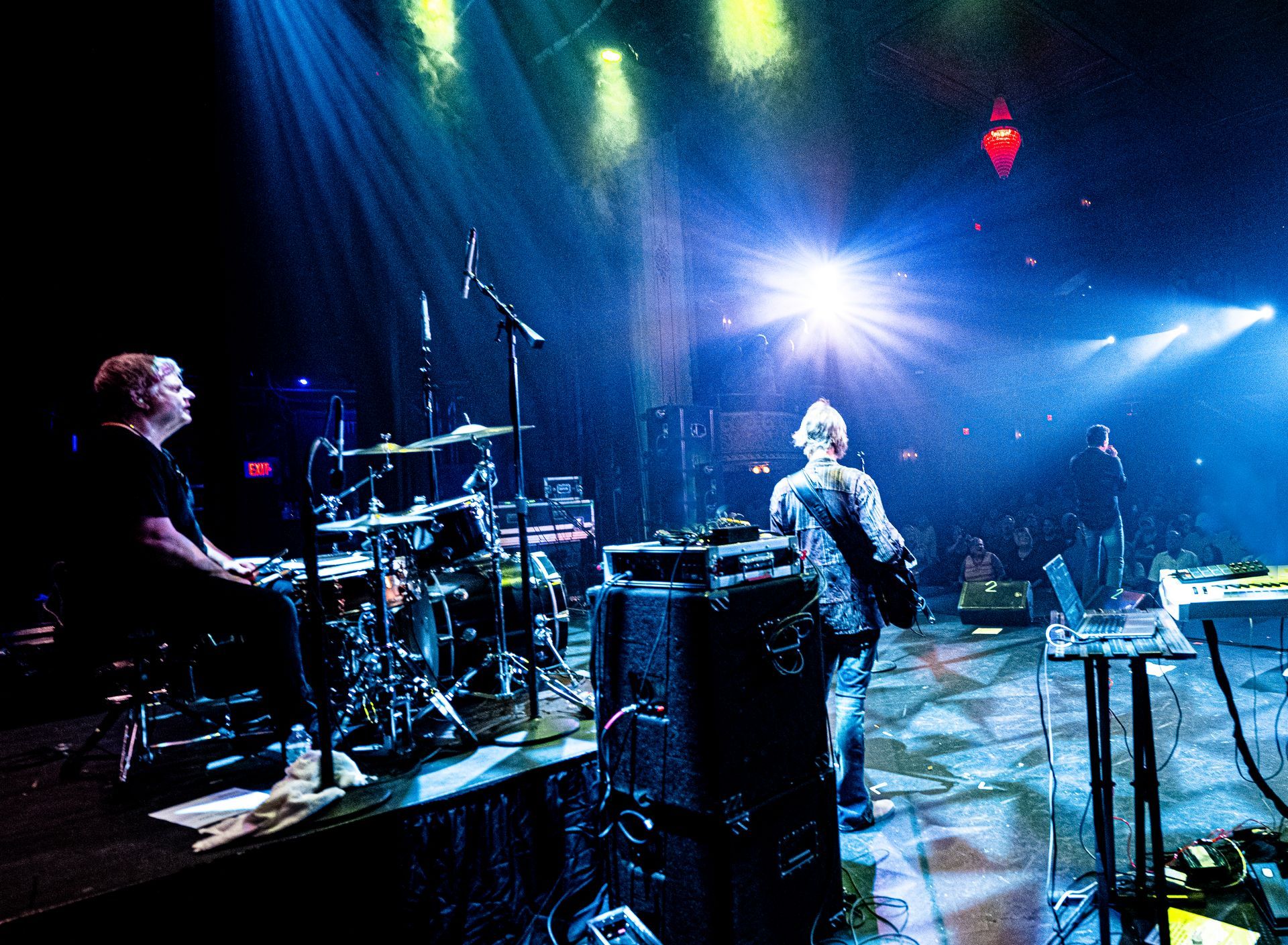 Band performing on stage, drummer on the left, guitarist in the middle, bright stage lights.