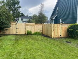 Wooden fence enclosing a backyard with green grass, a house, and gates.