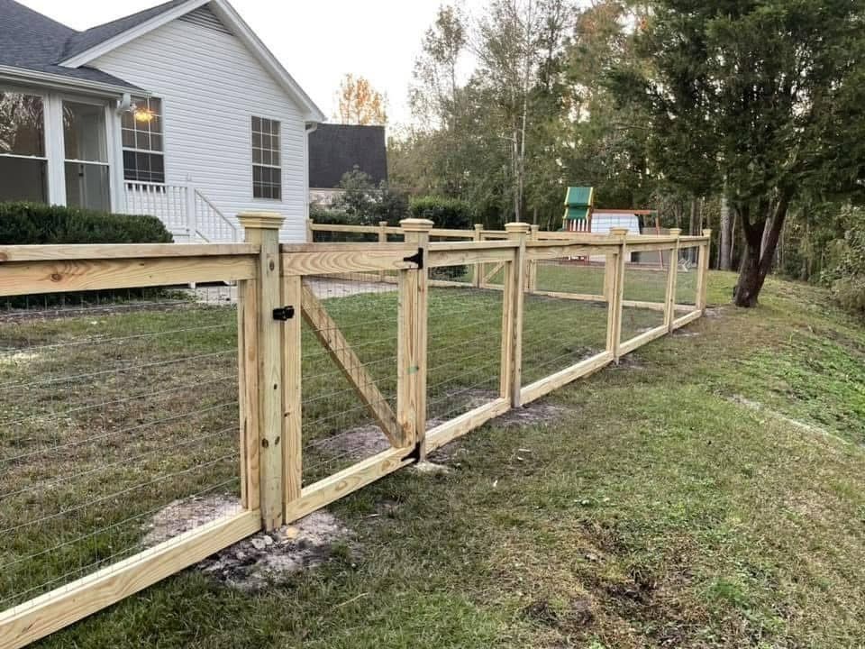 Wooden fence with gate in a yard next to a white house; a child’s play area is in the background.