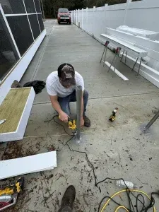 A man using a power tool on a metal pole outdoors, surrounded by construction materials.