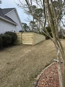 Wooden horizontal slat fence beside a house on a grassy lawn.
