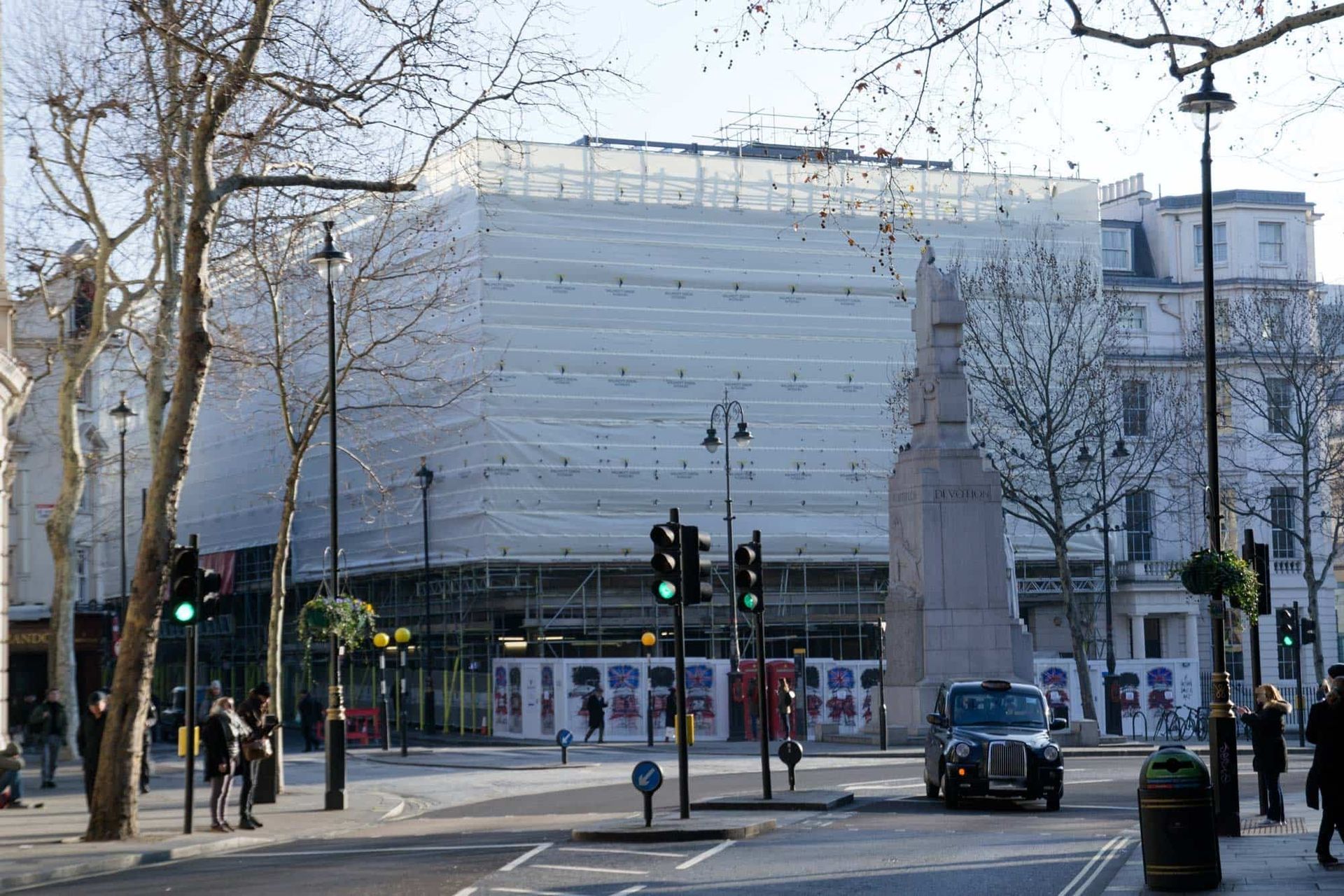 Building wrapped in white sheeting, under construction. Traffic light with green signal. Black taxi.