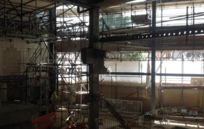 Interior view of a building under construction, scaffolding surrounding columns and walls.