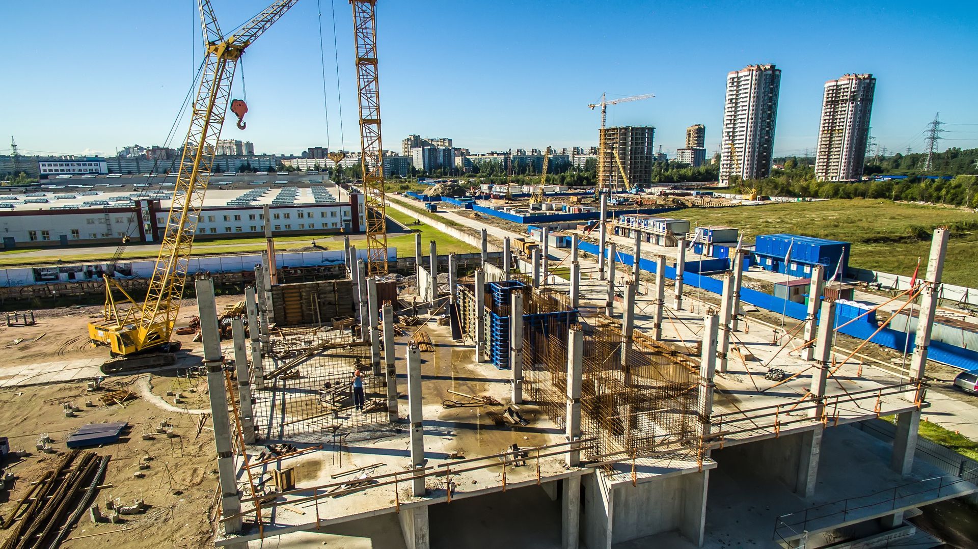 Construction site with cranes, concrete pillars, and partially built structures under a clear blue sky.