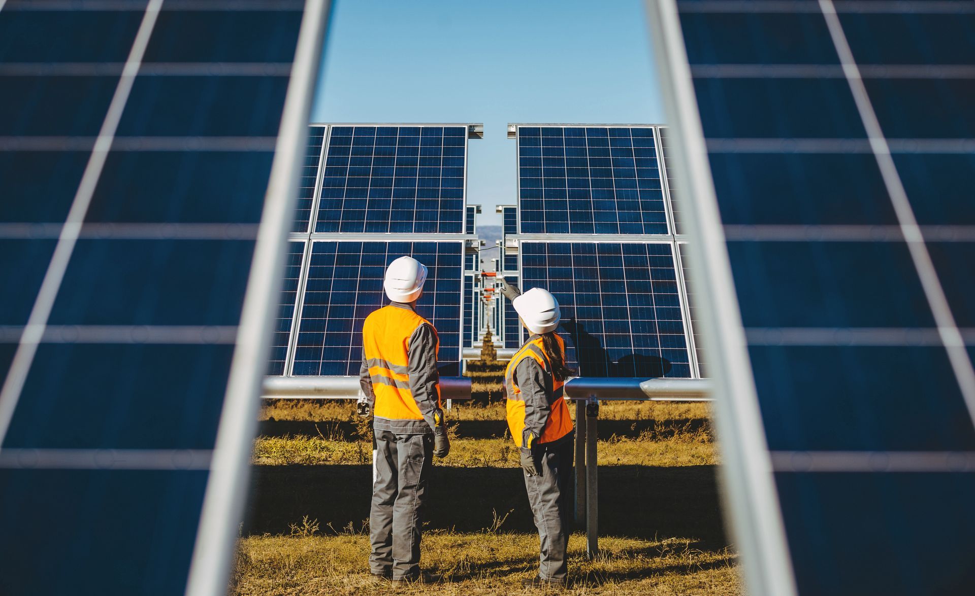 Two workers in safety vests and hard hats examining solar panels outdoors.