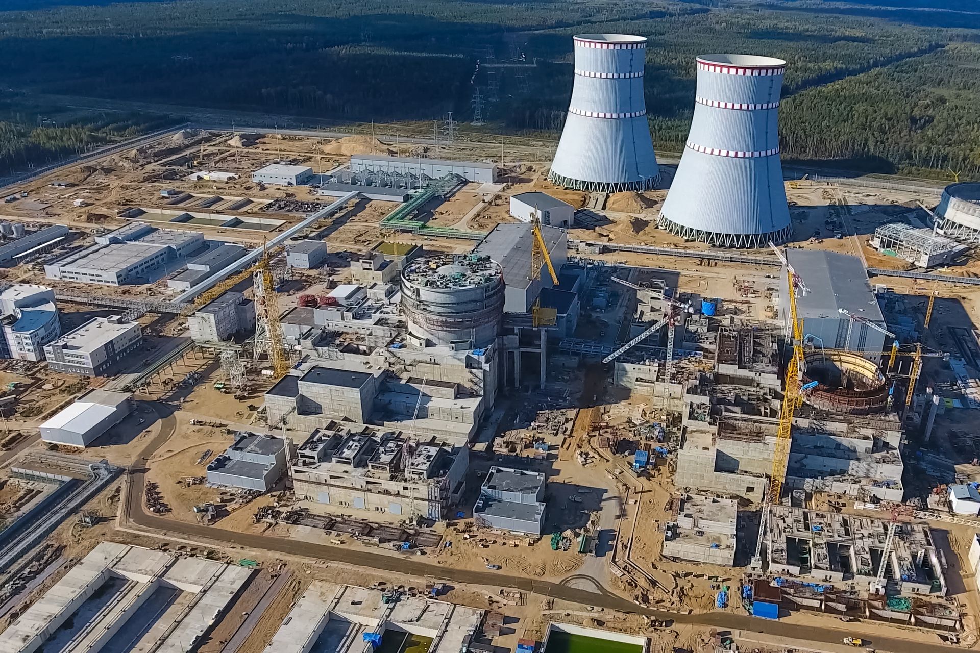 Aerial view of a nuclear power plant under construction. Grey buildings, two cooling towers, and construction equipment.