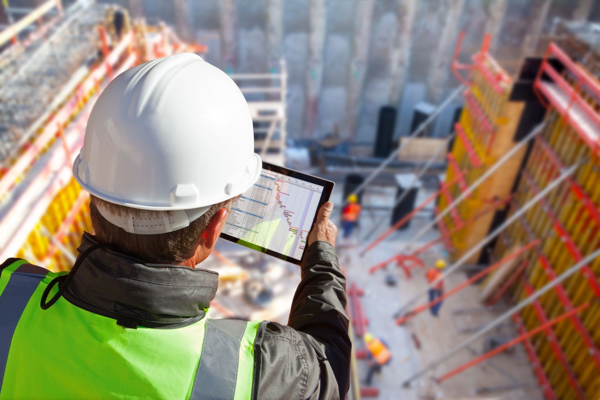 A construction worker is looking at a tablet at a construction site.