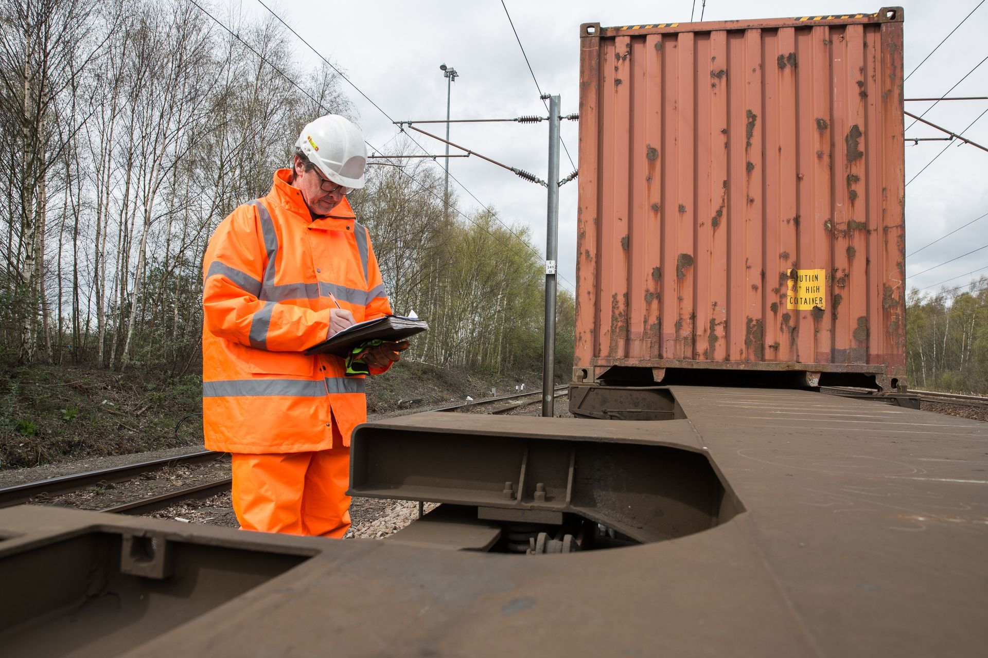 A man is standing on a train track looking at a clipboard.