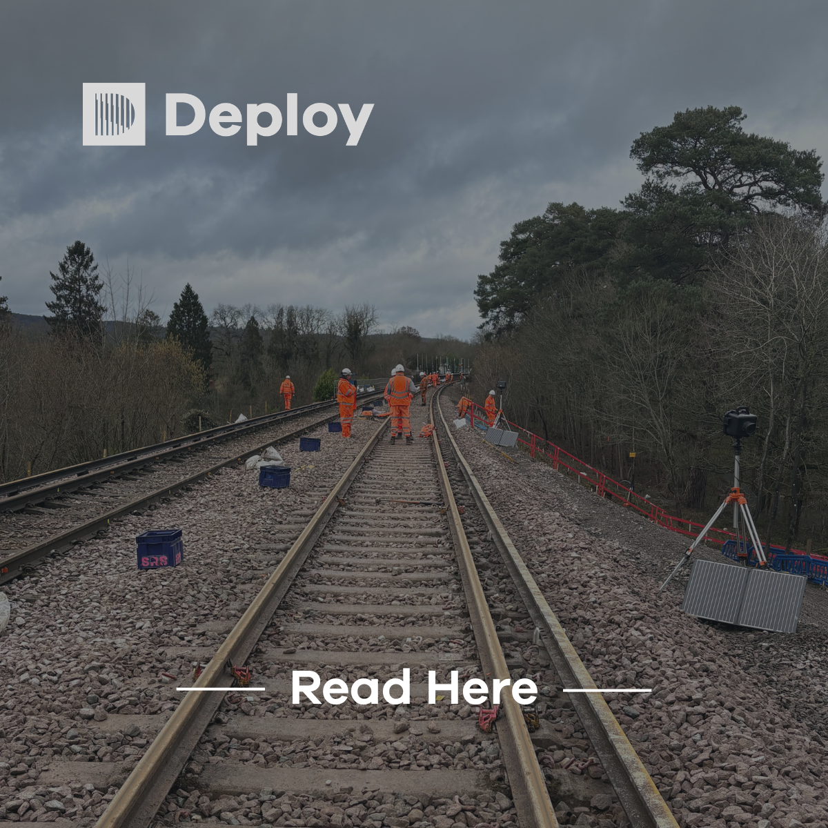 Railway workers in orange vests working on train tracks. Grey overcast sky.