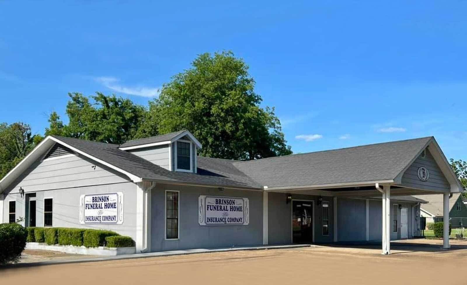 Single-story gray building with a covered drive-through and signs under a bright blue sky