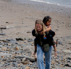 An Otra Cosa volunteer giving a piggy-back to a child across the beach at Huanchaco, Peru.