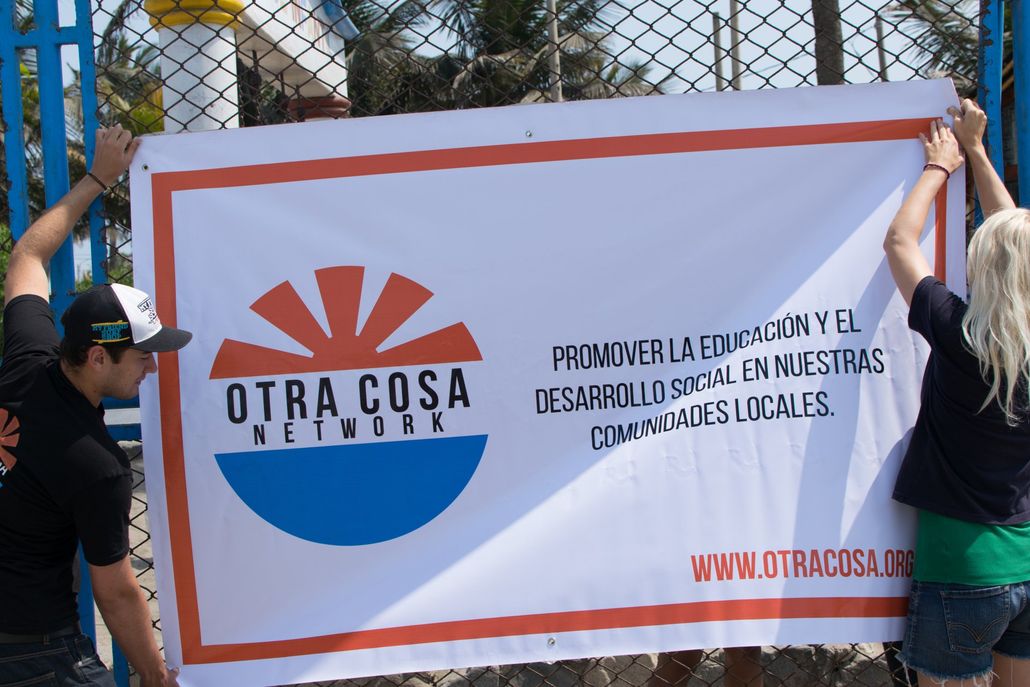 2 Otra Cosa volunteers hanging a promotional sign in Huanchaco, Peru.