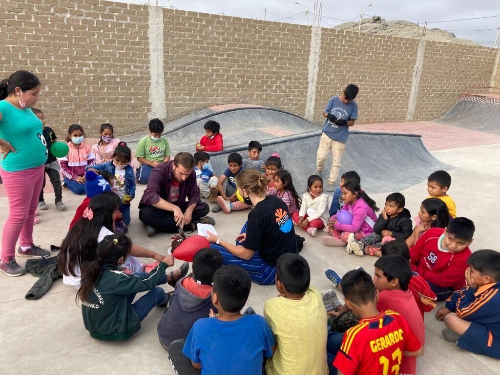 A group of Otra Cosa volunteers delivering a lesson to a large group of children at a skate ramp