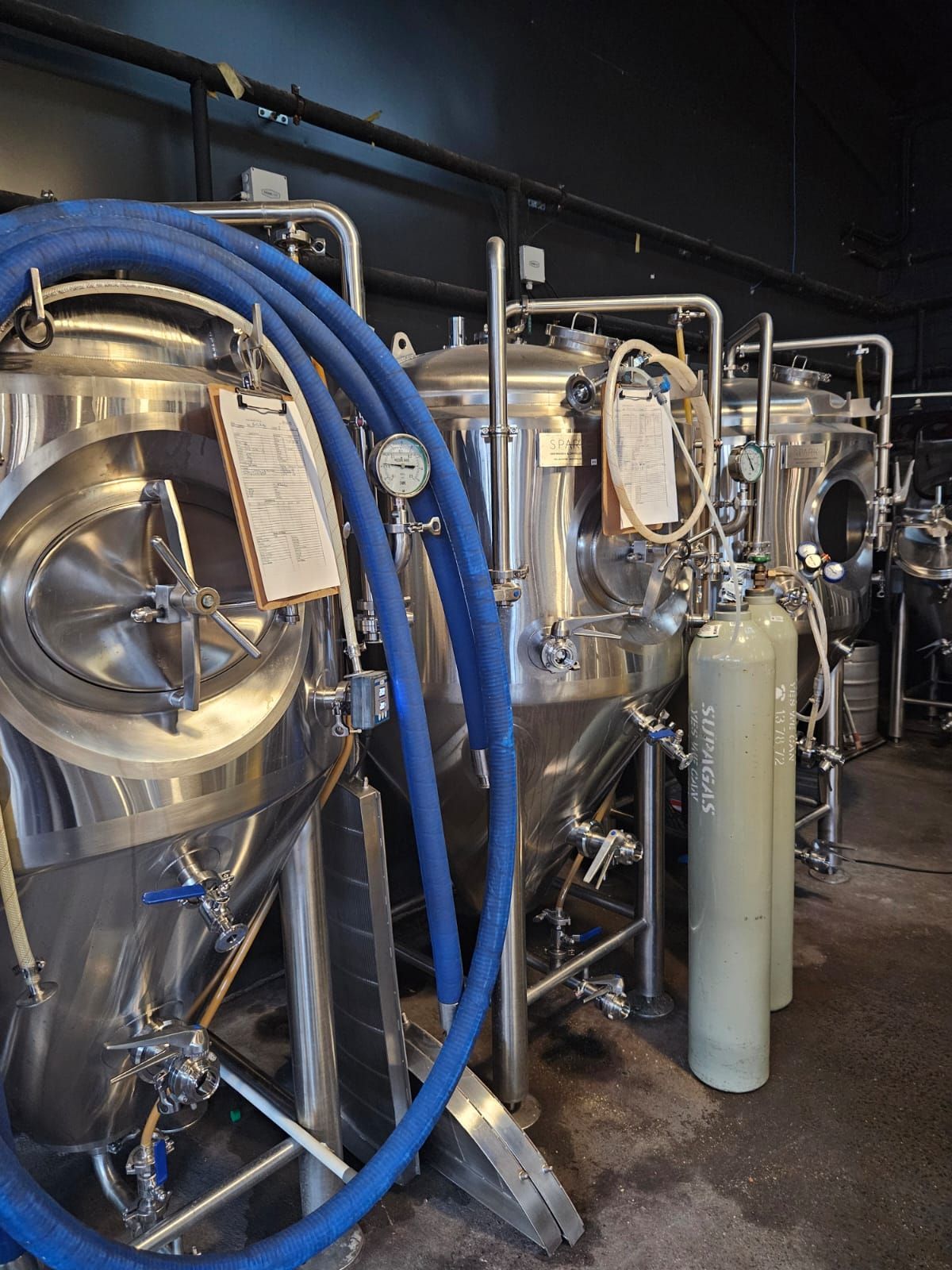 Stainless steel brewing tanks with blue hoses and a grey carbon dioxide tank.