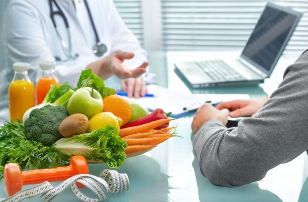 Arzt und Patient beraten sich über die Ernährung. Frisches Obst und Gemüse, Laptop, Maßband, Gewichte auf dem Tisch.