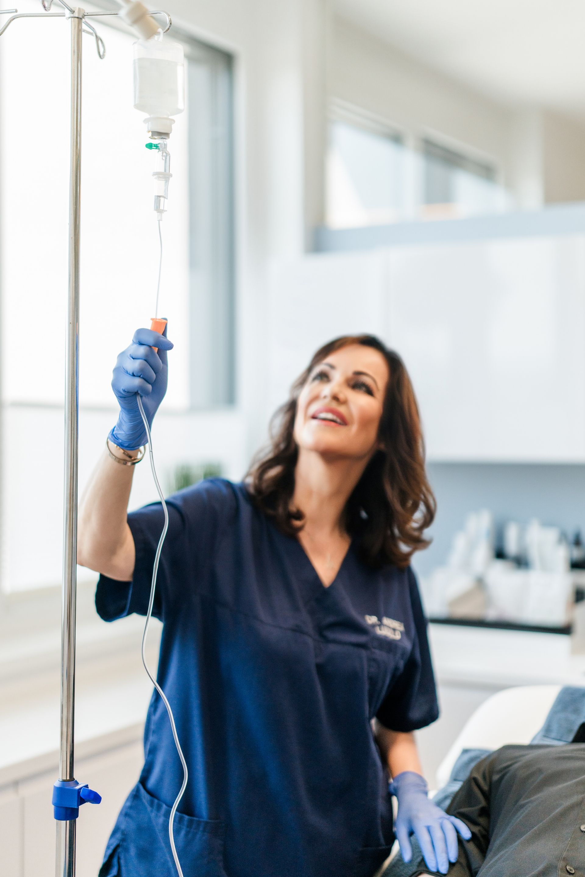 Ärztin passt Infusionsbeutel in heller medizinischer Umgebung an. Sie trägt Handschuhe und lächelt.