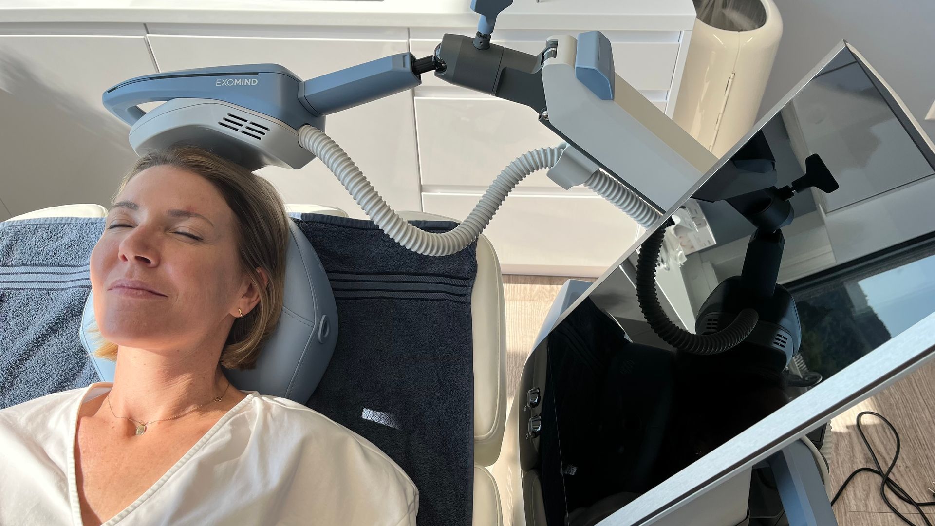 Frau erhält transkranielle Magnetstimulationbei EXOMIND-Behandlung; medizinisches Gerät über ihrem Kopf positioniert.