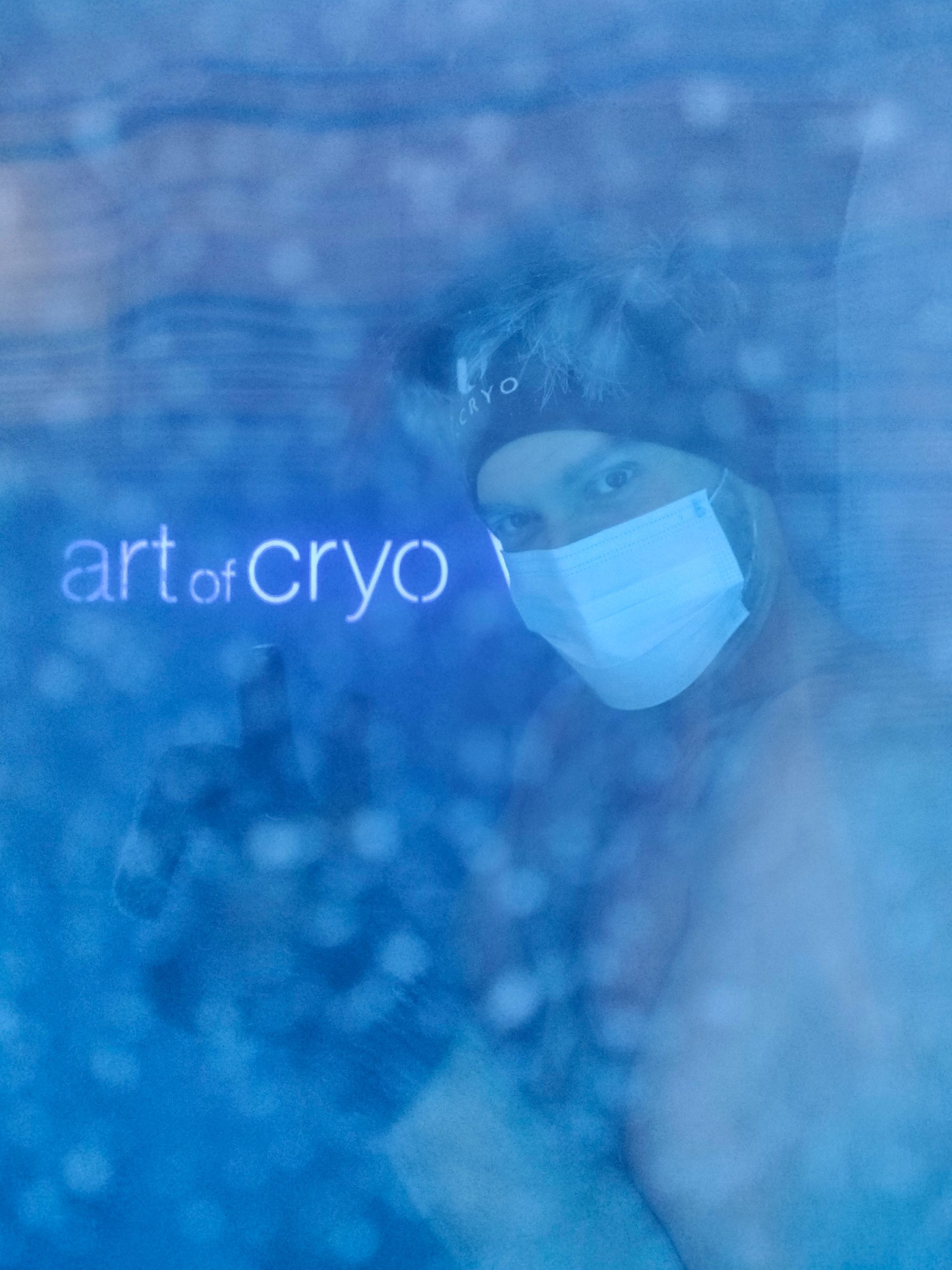 Person in der Kryotherapiekammer mit Maske, das Logo „Art of Cryo“ ist sichtbar.