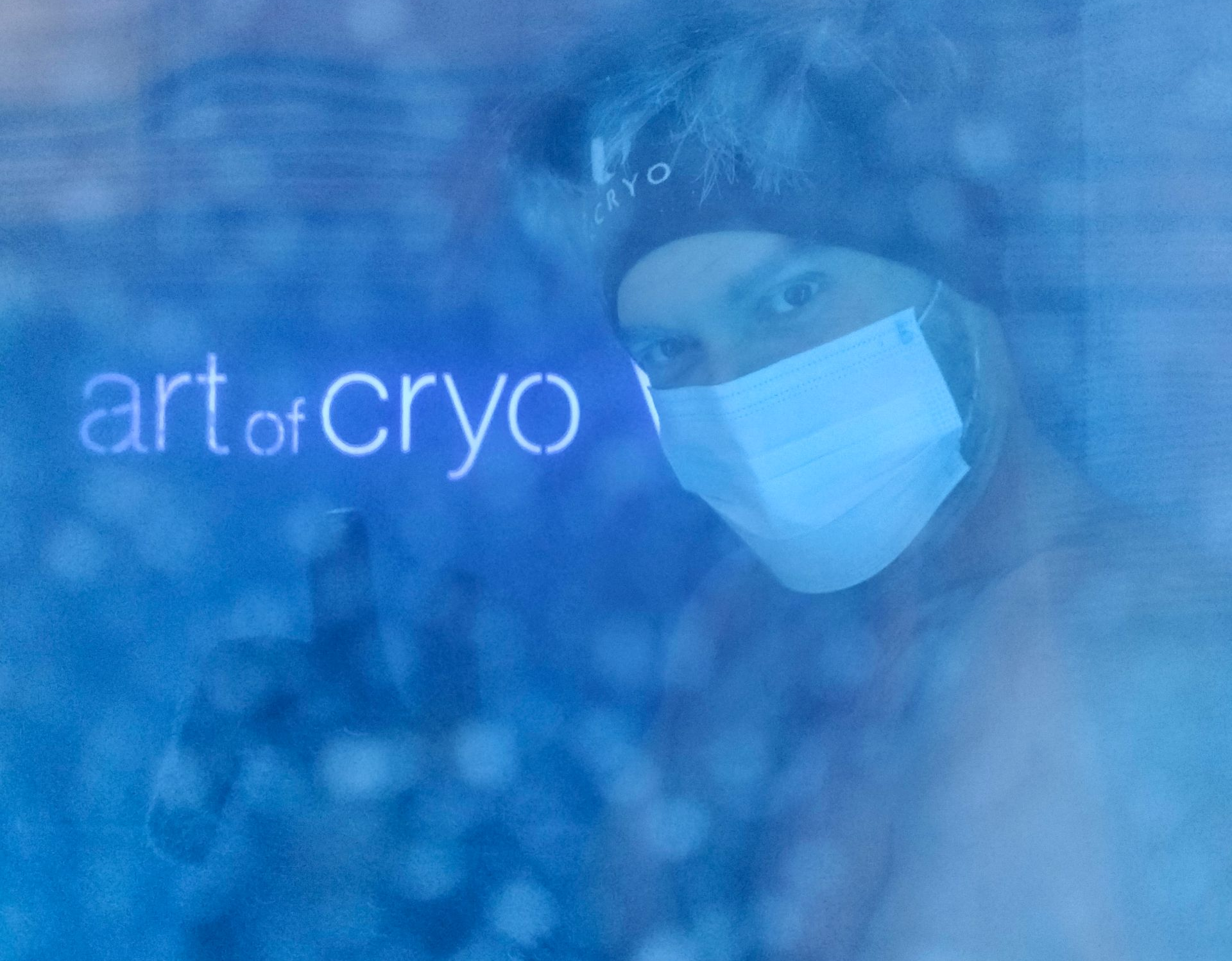 Mann mit Maske und Mütze in der Kryotherapiekammer; blau getönt, Text „Art of Cryo“ sichtbar.