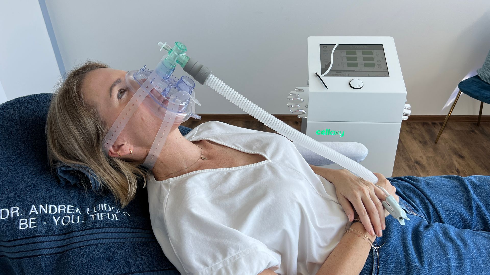 Frau mit Sauerstoffmaske liegt auf einem Bett, angeschlossen an eine Maschine in einer Klinik.