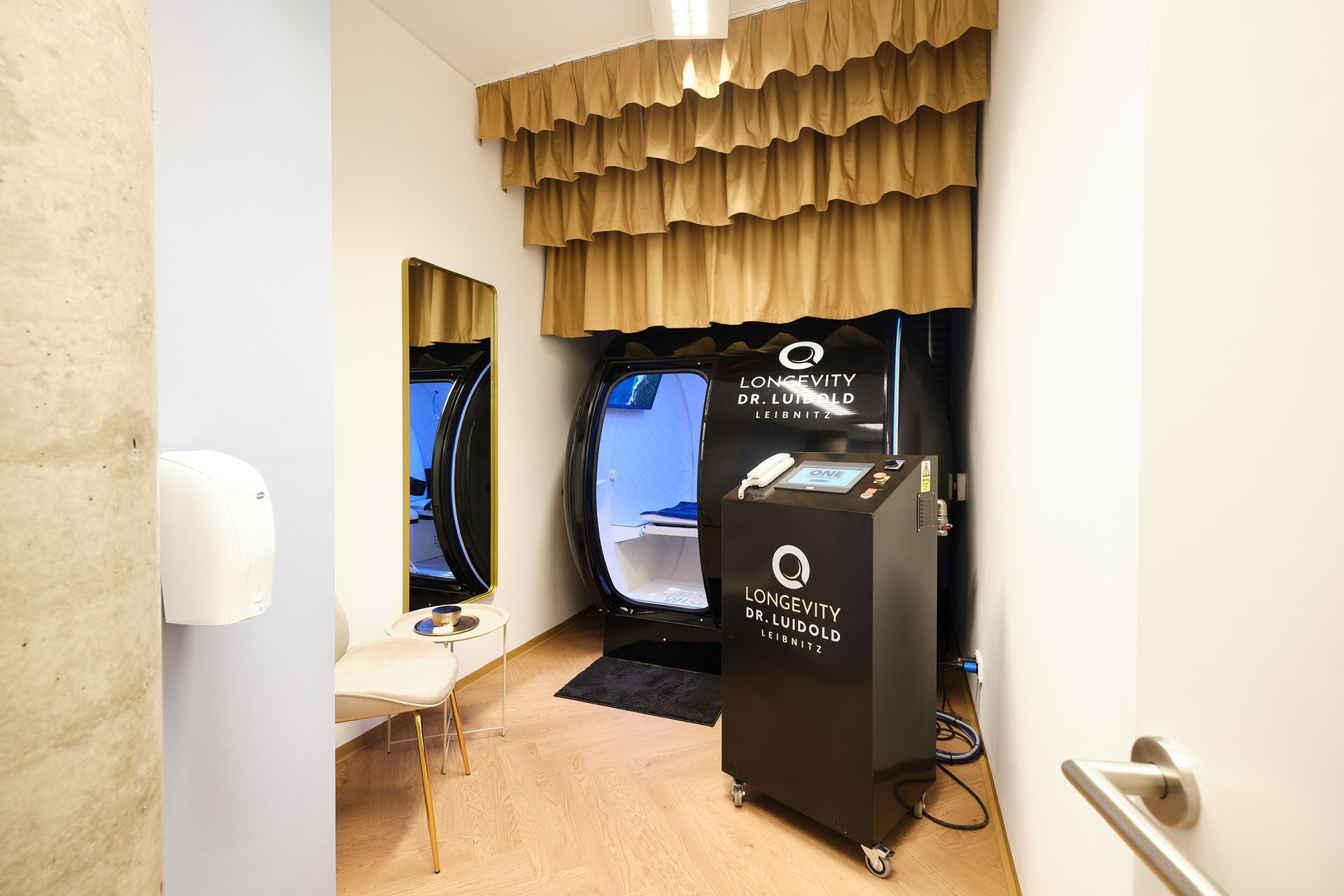 Schwarze Kapsel für HBOT-Behandlung mit blauem Innenraum, Bedienfeld. „ONE HYPERBARICS“-Logo, 