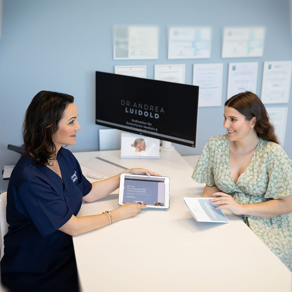 Dr. Andrea Luidold berät einen Patienten und zeigt ihm in einer Arztpraxis Informationen auf einem Tablet.