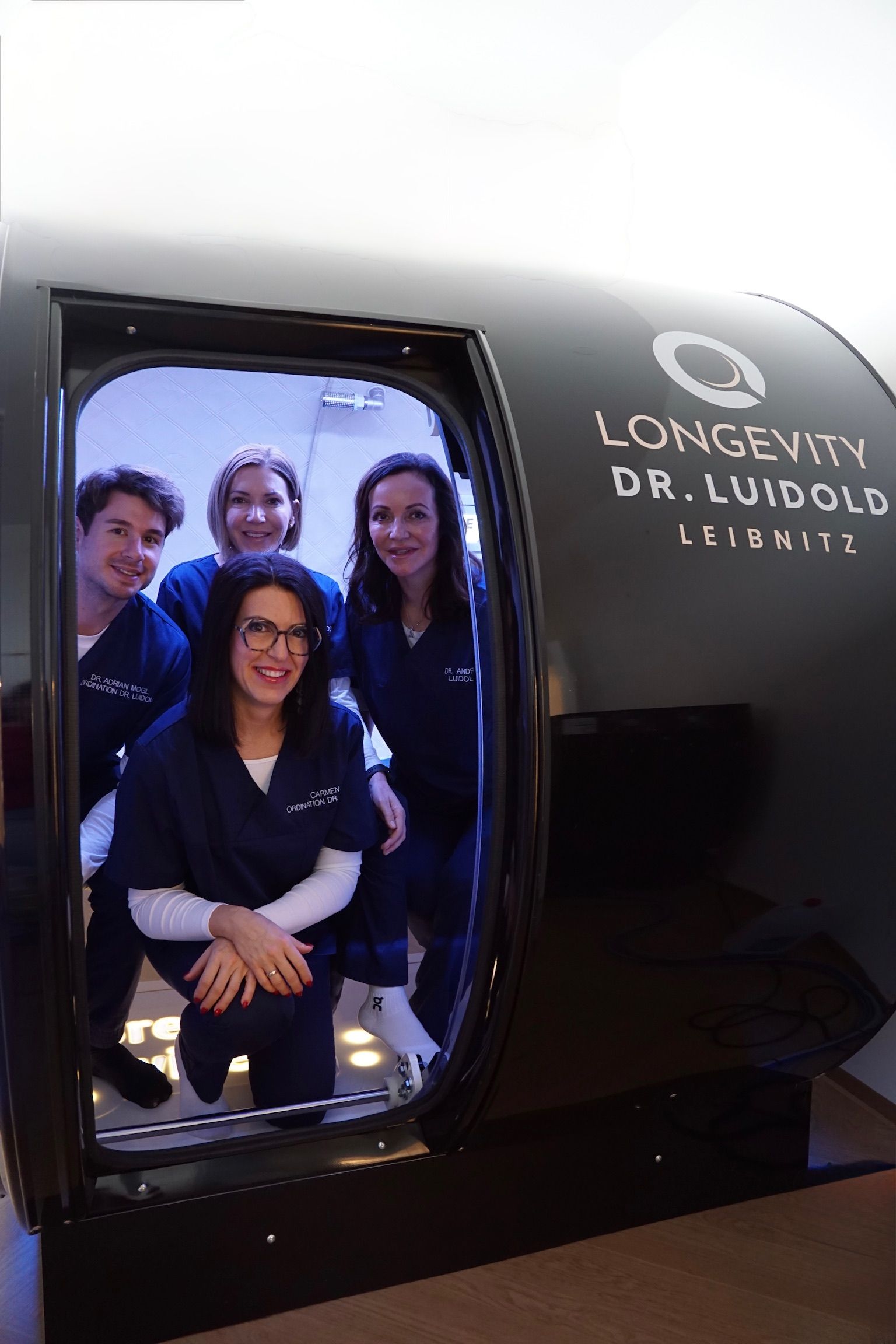 Fünf medizinische Fachkräfte in blauen Kitteln posieren im Innenbereich vor einer hellen Wand.