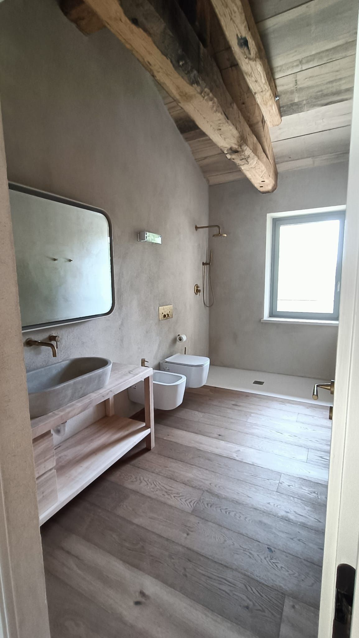Piccolo bagno rustico con travi in legno, specchio, lavandino, WC e finestra.