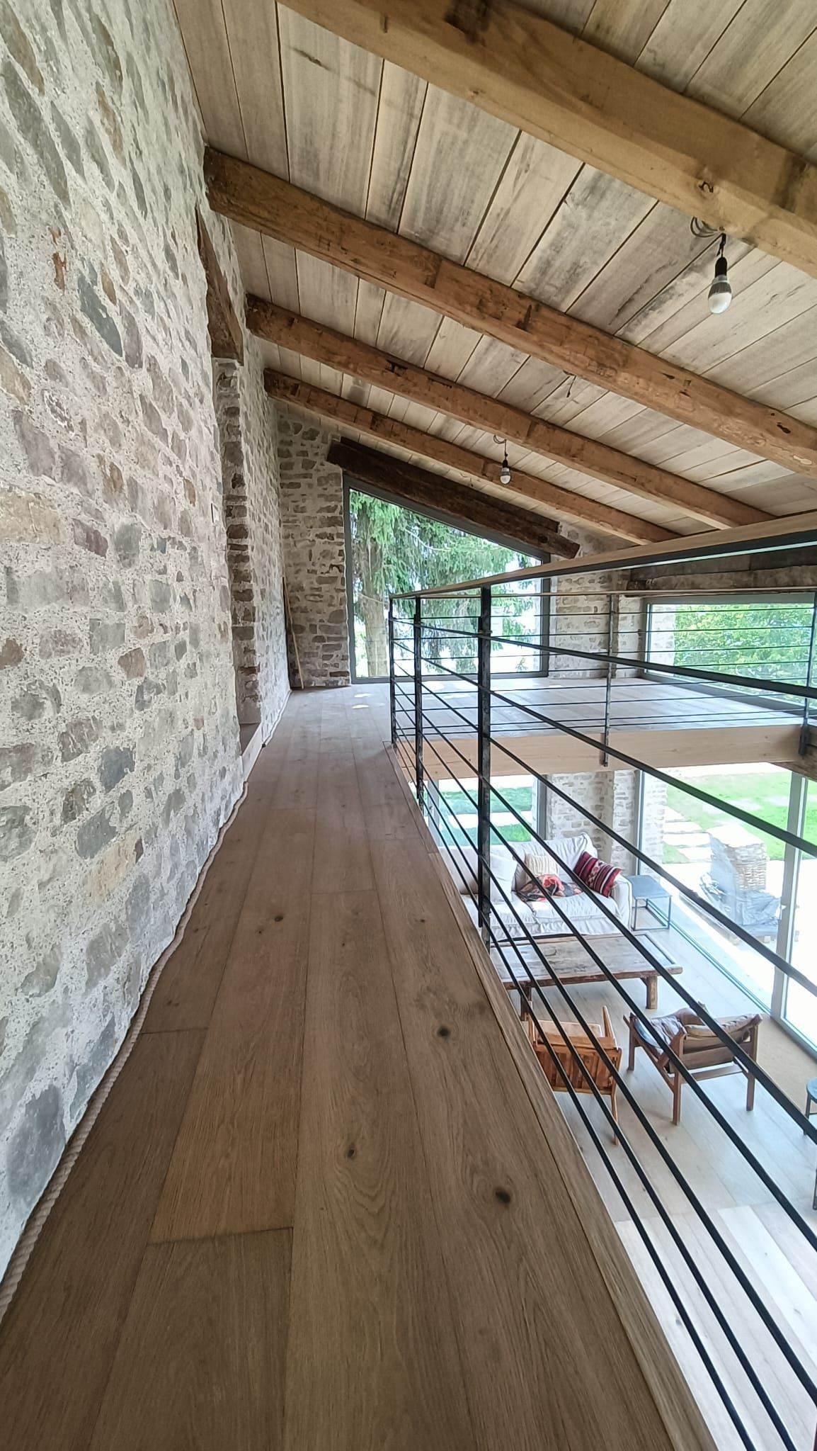 Passerella in pietra con travi in legno e ringhiera in metallo che si affaccia sul verde.
