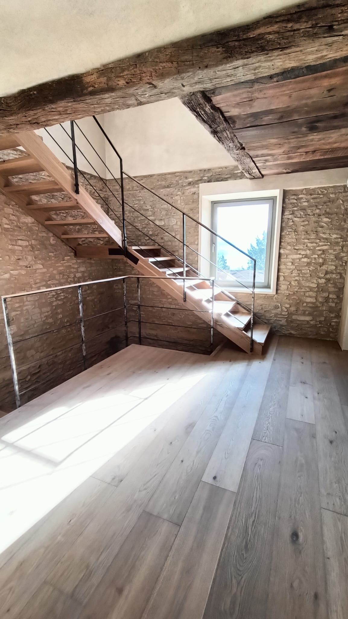 Mansarda rustica vuota con travi in legno, scala, pavimento bianco e finestra.