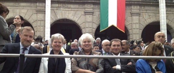 Eine Gruppe von Menschen sitzt vor einem Gebäude mit einer Flagge im Hintergrund.