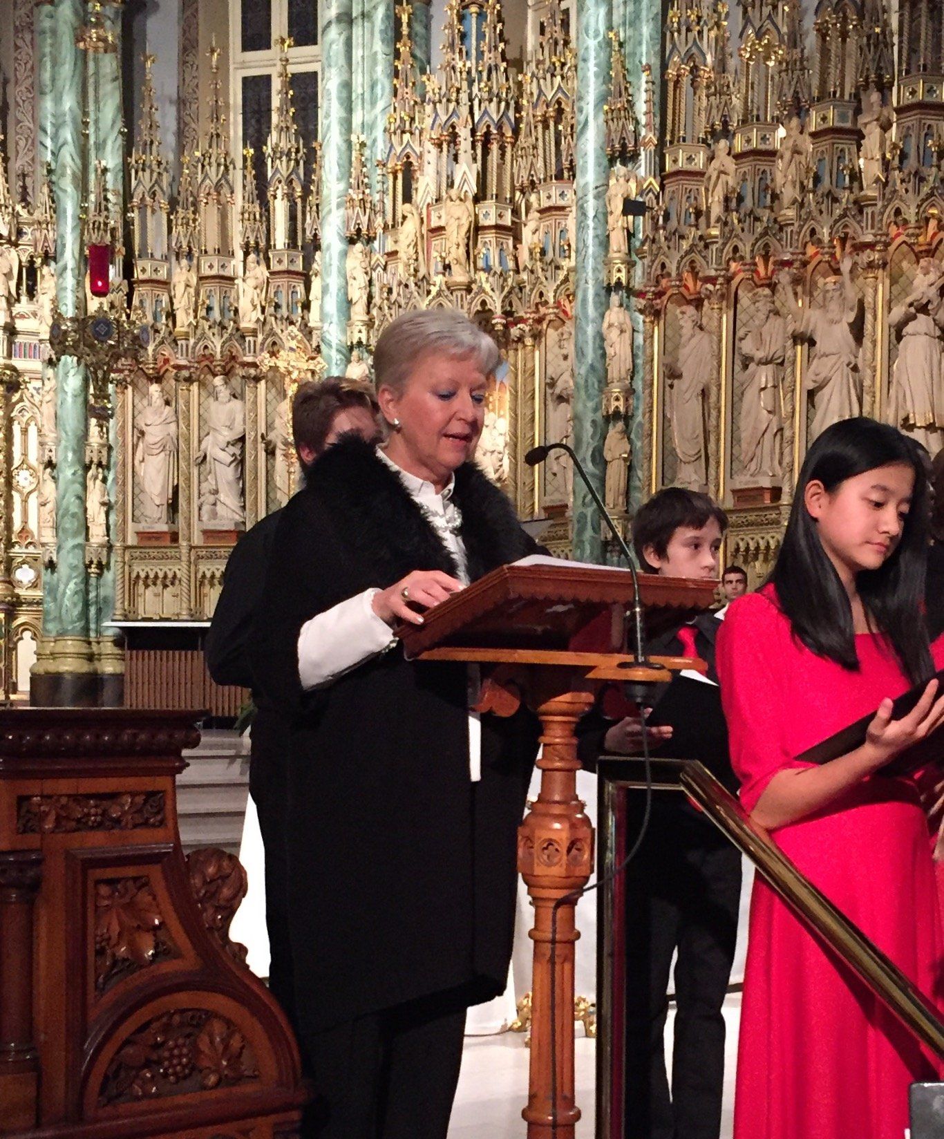 Eine Frau steht an einem Podium und liest einer Gruppe von Kindern ein Buch vor