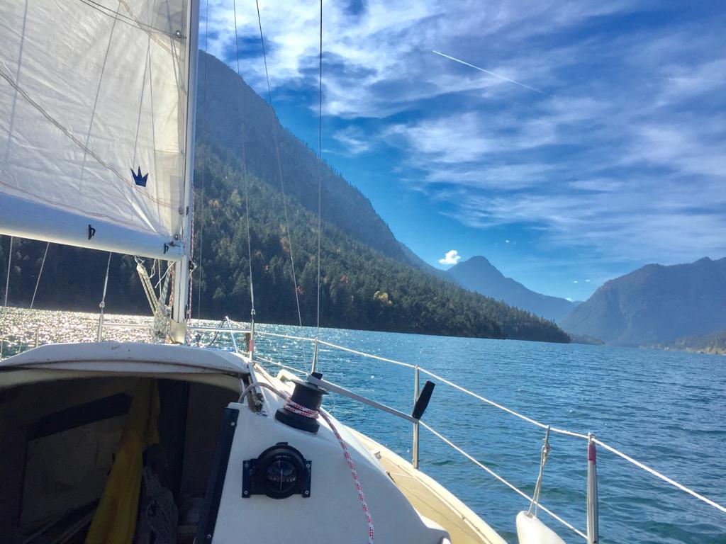 Ein Segelboot schwimmt auf einem See mit Bergen im Hintergrund.
